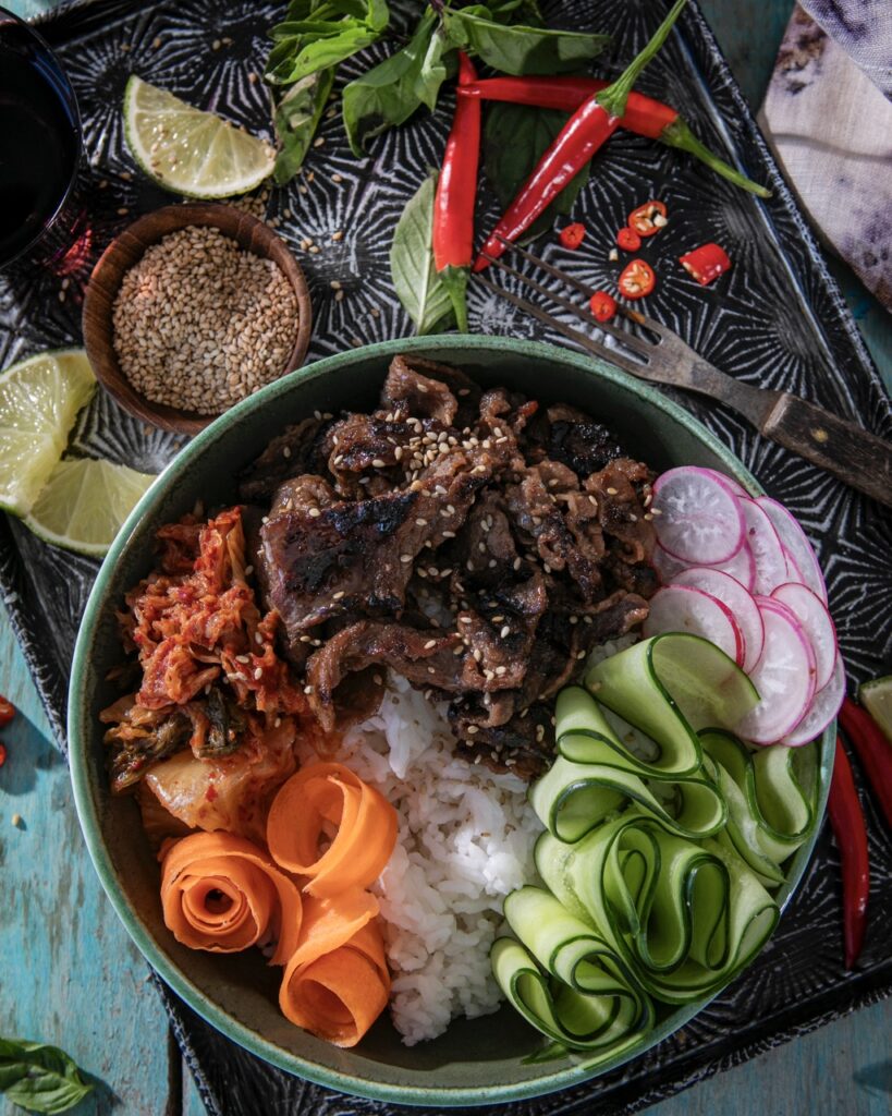 A beef bulgogi bowl with rice, cucumbers, radishes, carrots, and beef.