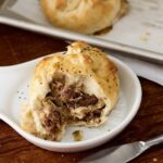 Partially eaten Beef and Caramelized Onion Knishes served on a ceramic plate with a knife on the side.