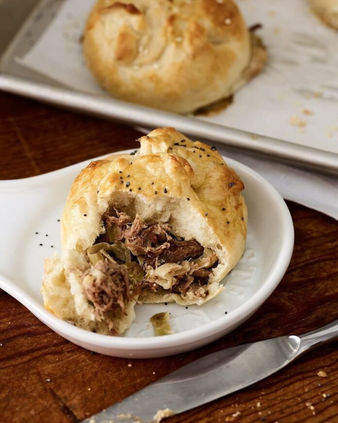 Partially eaten Beef and Caramelized Onion Knishes served on a ceramic plate with a knife on the side.