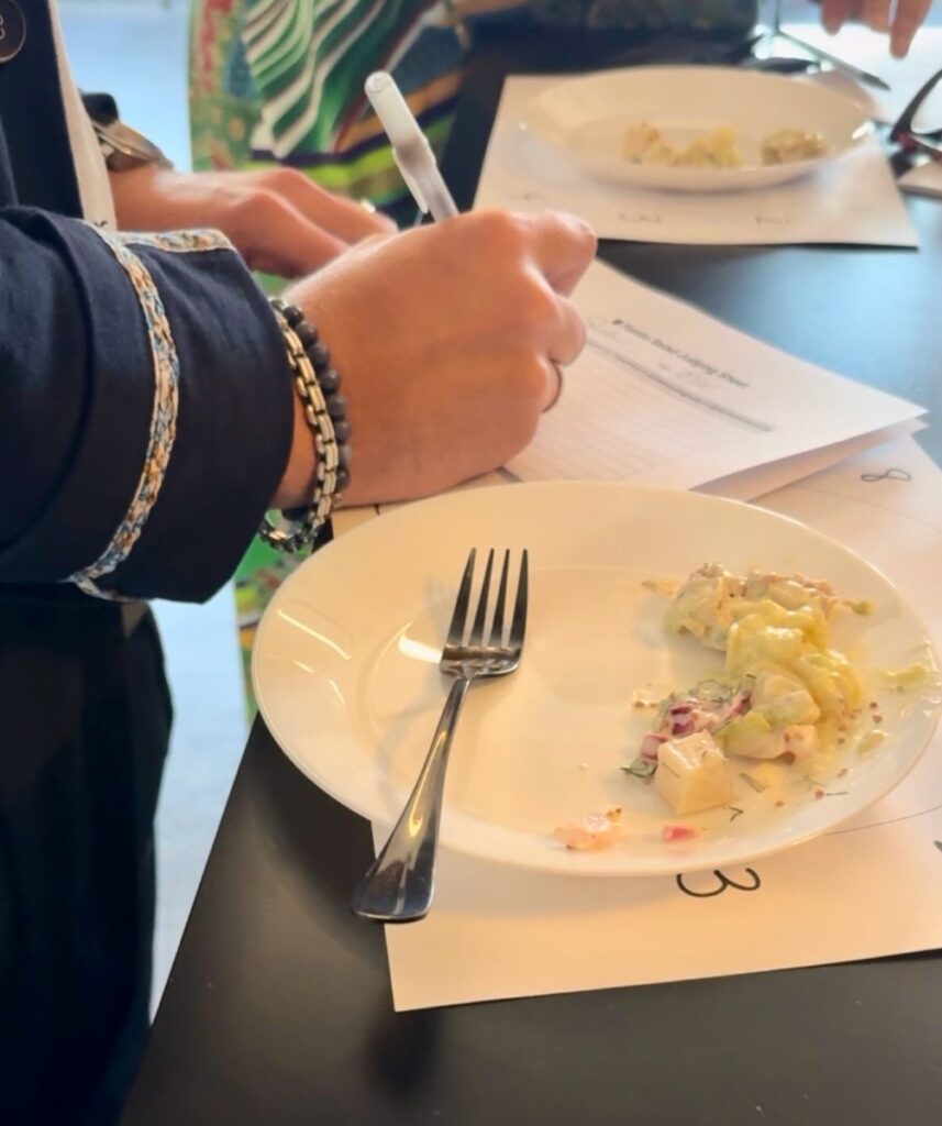 A person writes on a sheet of paper next to a white plate of potato salad.
