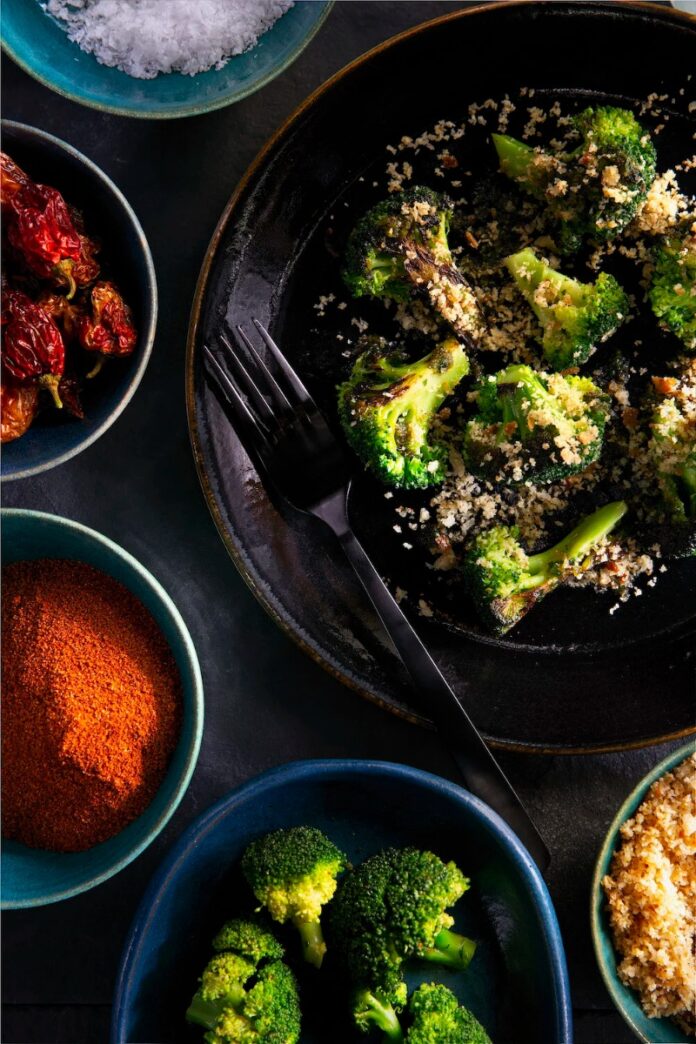 Broccoli, Brown Butter Bread Crumbs A plate of roasted broccoli florets with brown butter bread crumbs, surrounded by bowls of salt, red pepper flakes, paprika, and more broccoli.