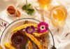 Best Corn Recipes On and Off the Cob A bowl of corn ribs sits on a wooden table with a small container of homemade BBQ sauce in the center. Two glasses of beer sit in the top right corner and flowers are scattered throughout.
