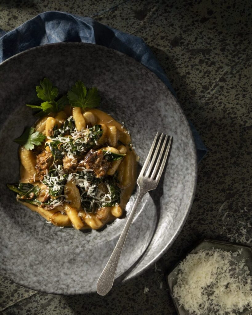 An aerial shot of a gray stone bowl filled with GNOCCHI WITH BRAISED OXTAIL AND COLLARD GREENS.