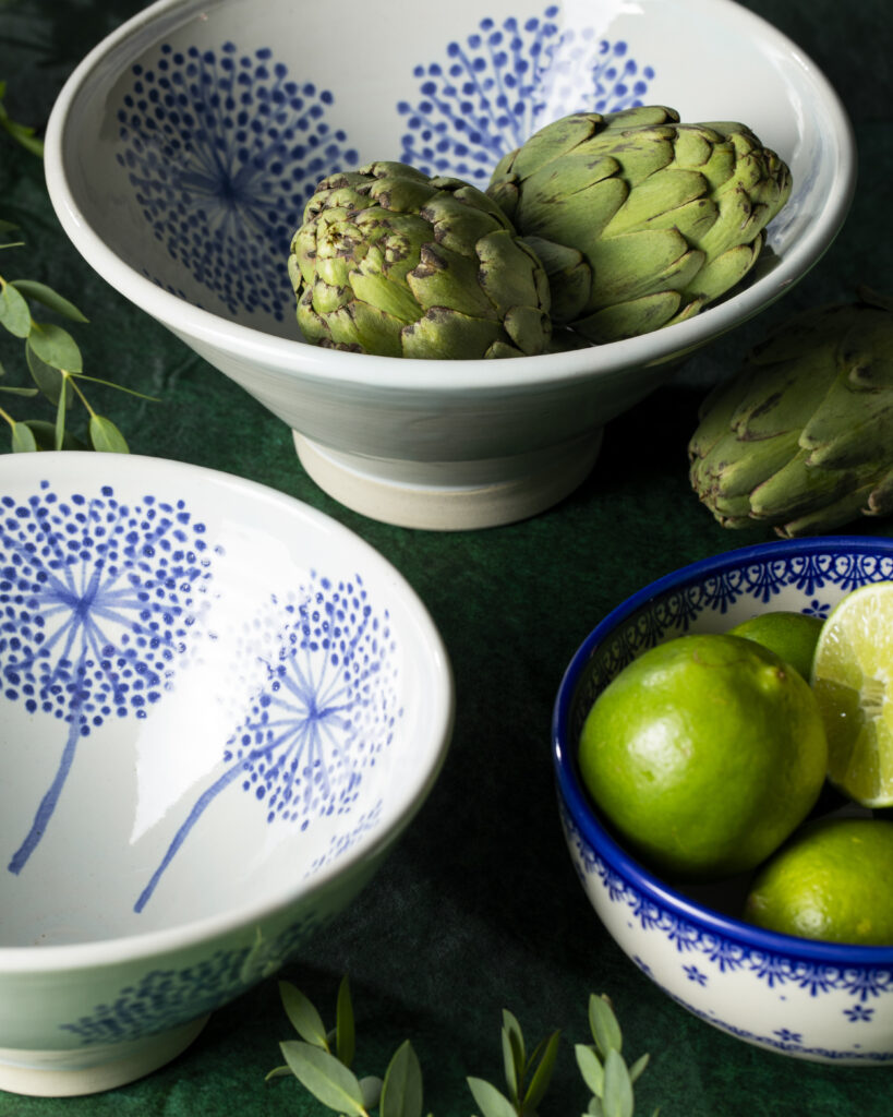 three white bowls with blue flower patterns. one bowl holds limes, another artichokes.