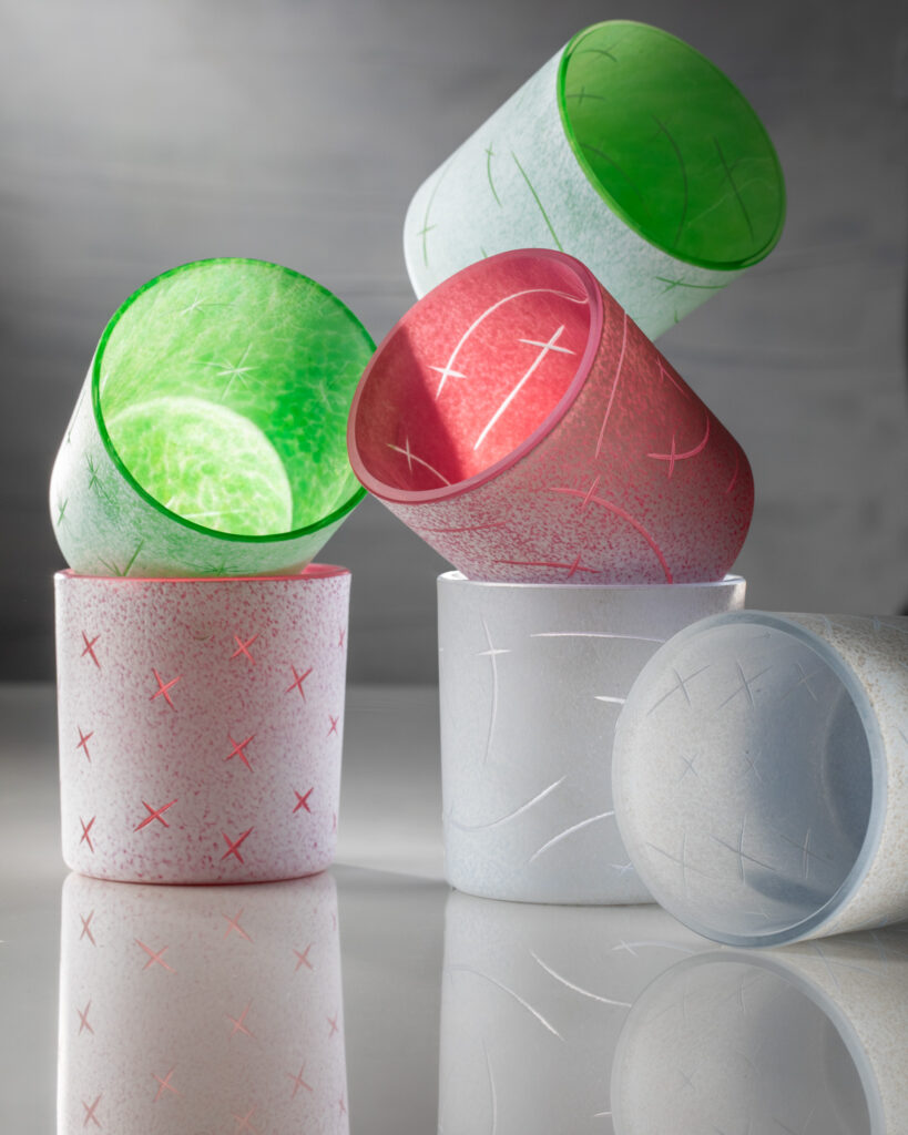 Six green and red handblown glass and engraved cups stand stacked on top of each other. tech pastels design