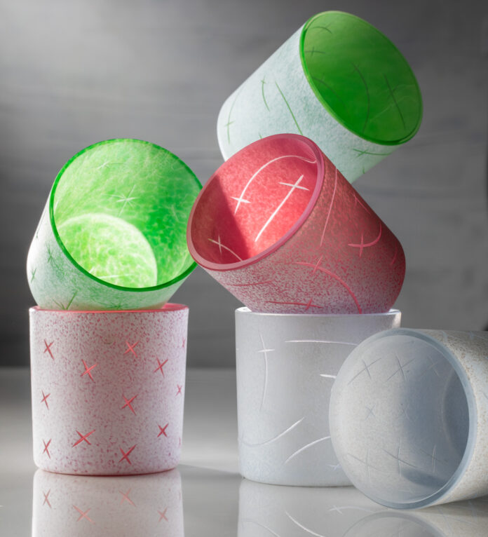 Six green and red handblown glass and engraved cups stand stacked on top of each other. tech pastels design