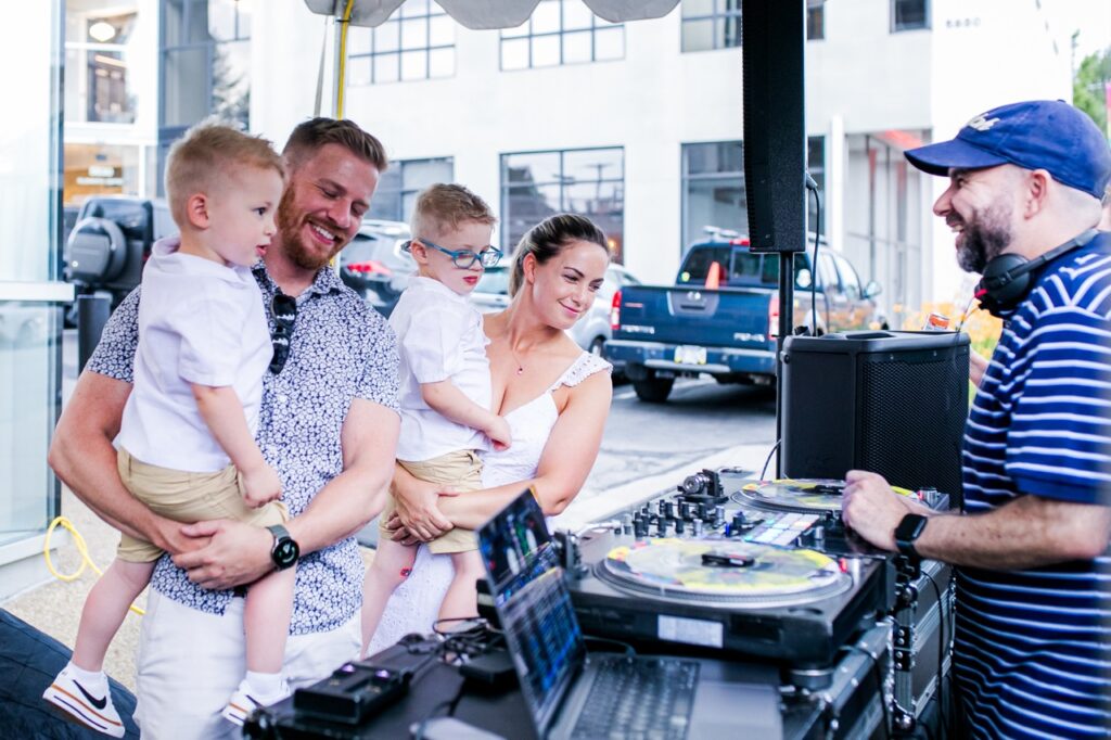 Two young boys and their parents look at the DJ booth.
