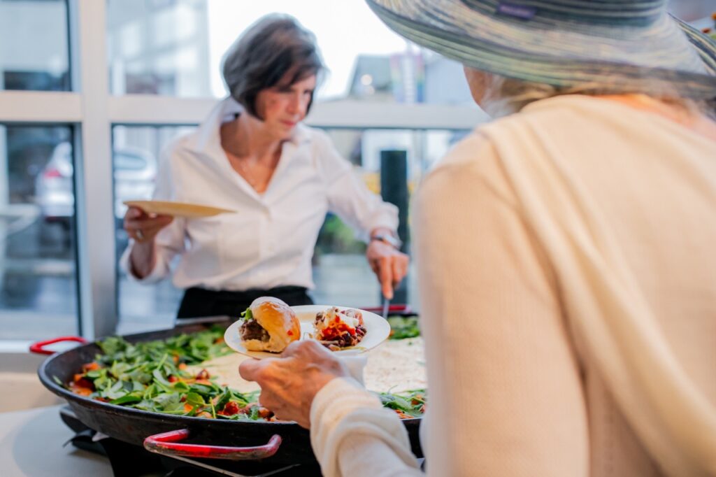 A woman scoops salad up for another.