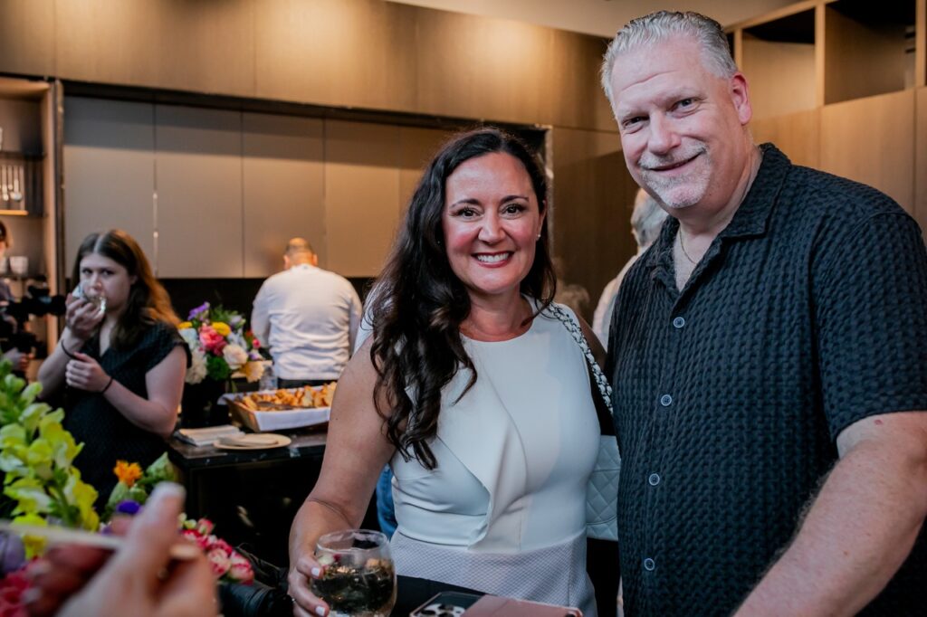 A man in a button up and woman in a white dress stand together.