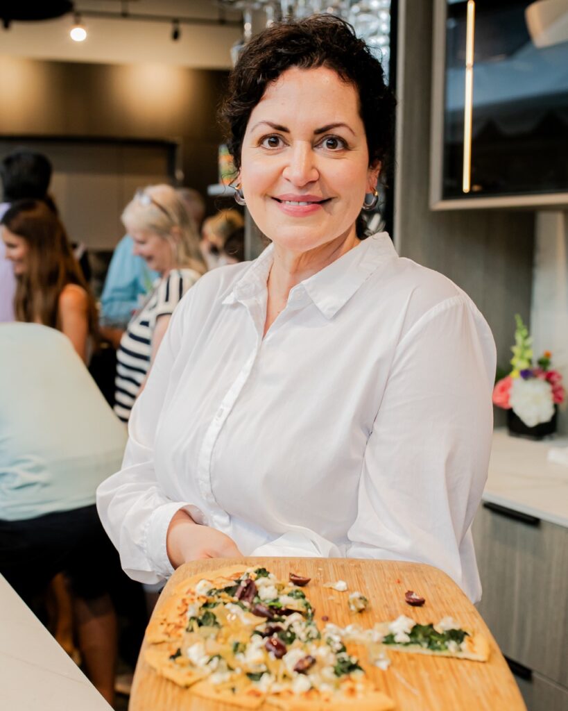 A woman holds out a cutting board of flatbread pizza.