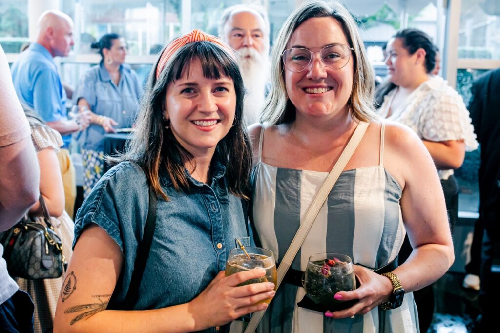 A woman in a jean dress and another in a striped dress stand together.