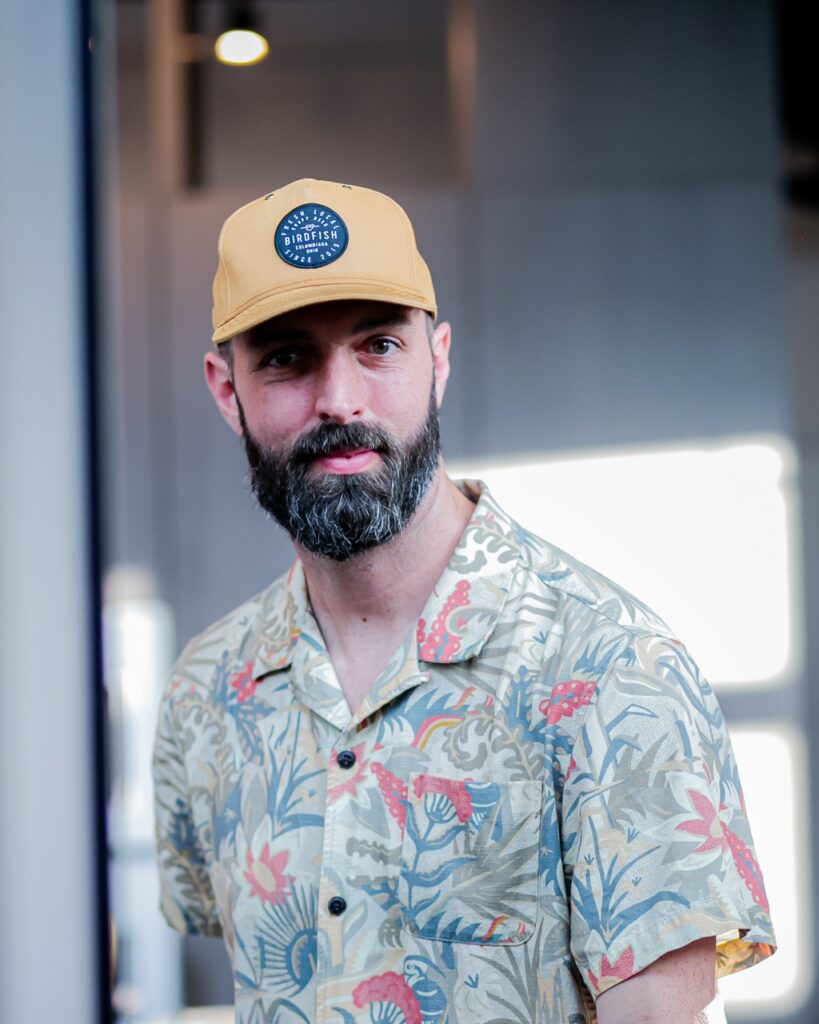 A man in a baseball hat looks at the camera.