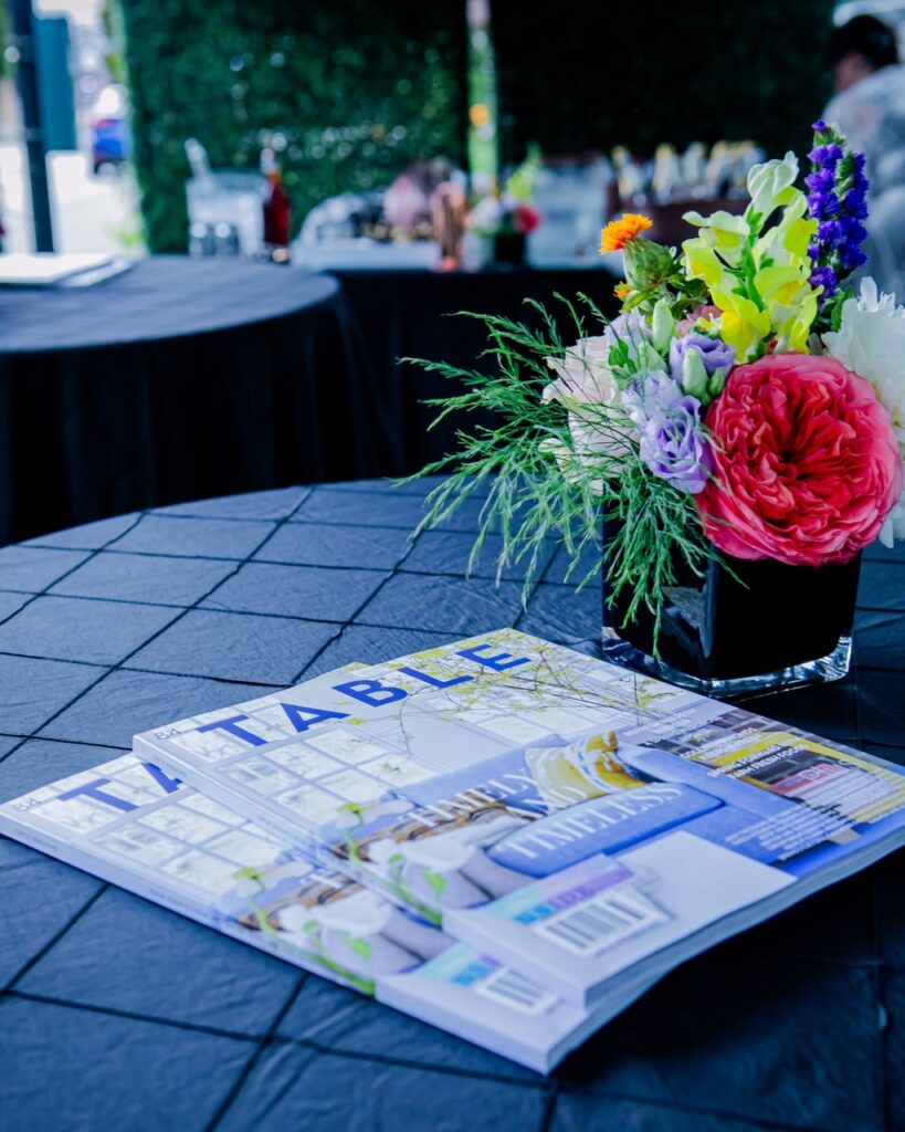 Two TABLE Magazine's sit on a table beside a flower arrangement.