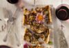 Eggplant and Smoked Mozzarella Tart An eggplant and smoked mozzarella tart cut into pieces on a white table beside silverware and plates.