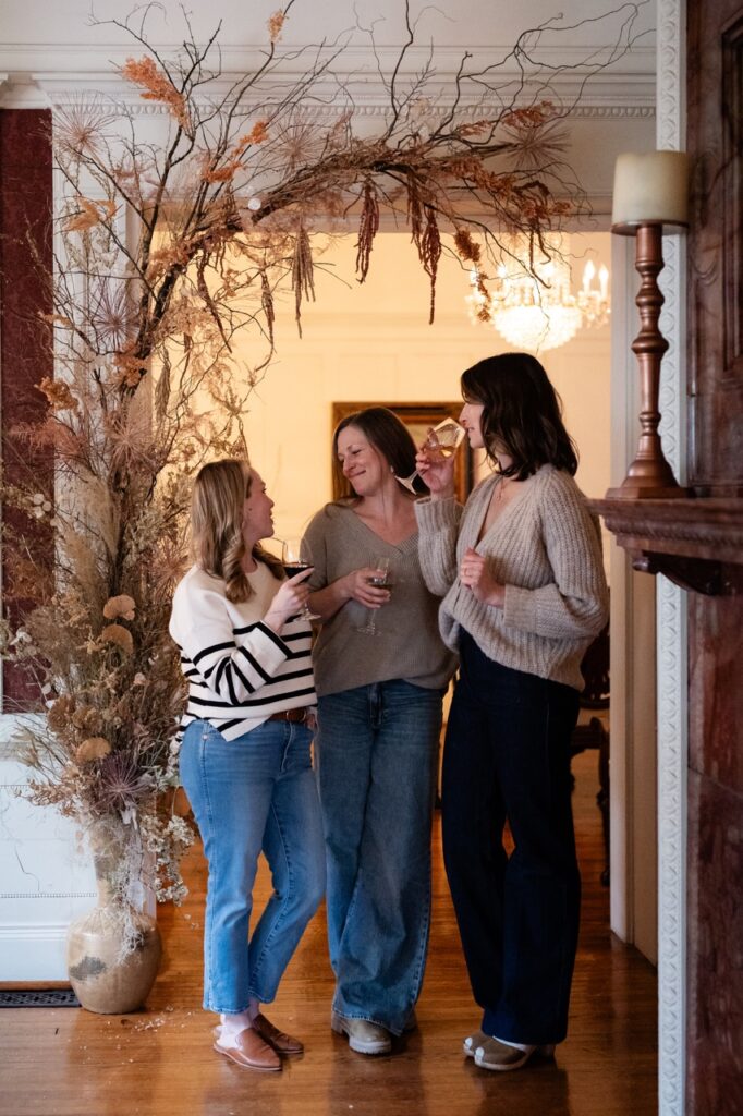 Three women laugh in the doorway of a home.