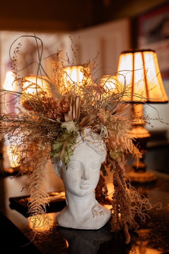 A greek woman statue with dried flowers coming out of it.