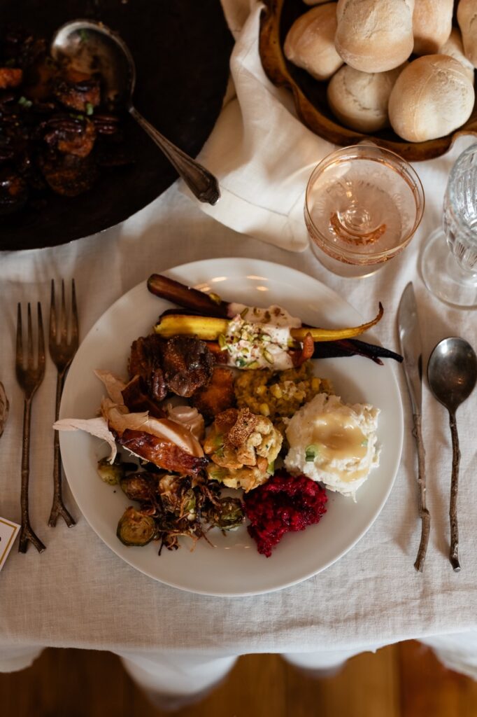 A plate full of friendsgiving food sits on a white table.