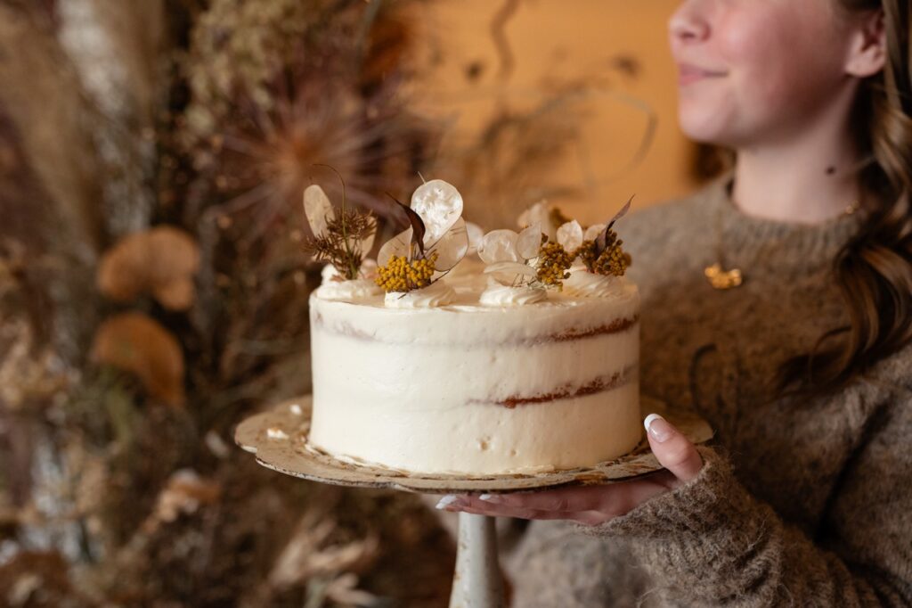 A girl holds a white frosted layer cake.