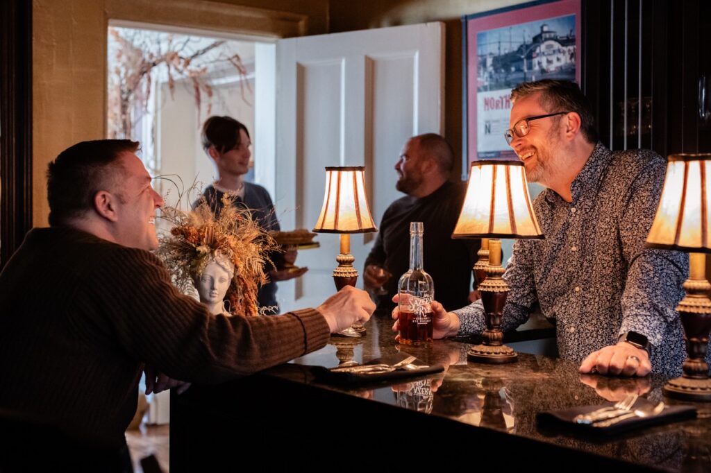 A man cheers with another across a lamp lit bar.