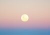 Your Full Moon in Aquarius Horoscope for August 2025 A full moon sits above the ocean rolling into the August sands as the sun sets.