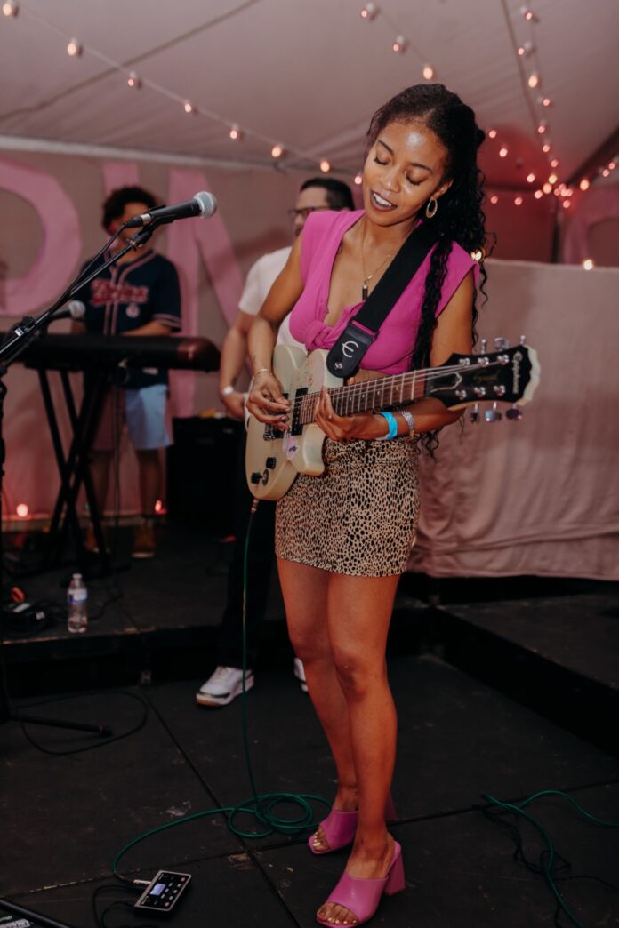 A woman in a pink top plays a white guitar on stage.
