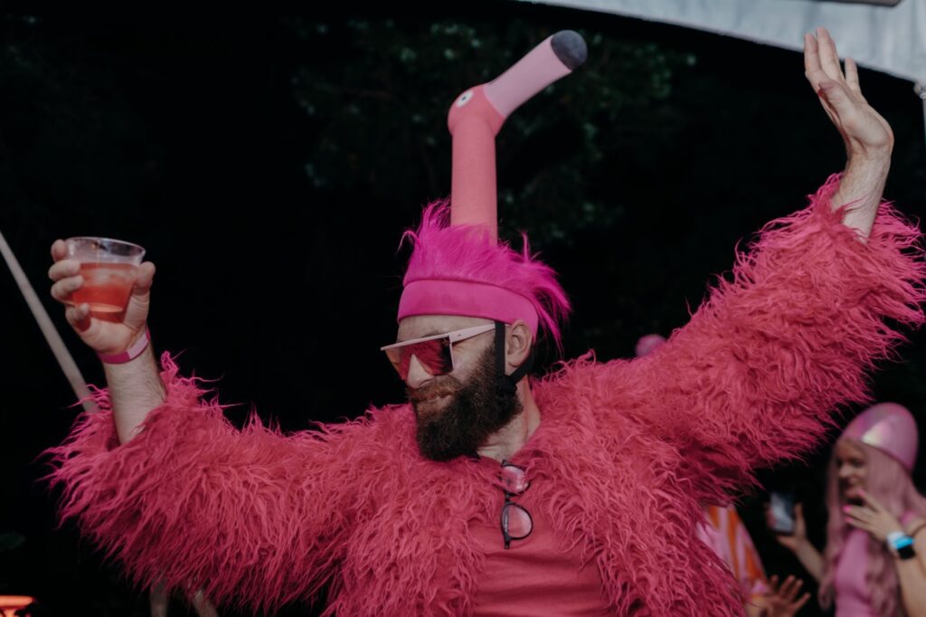 A man with a pink flamingo outfit holds up a drink.