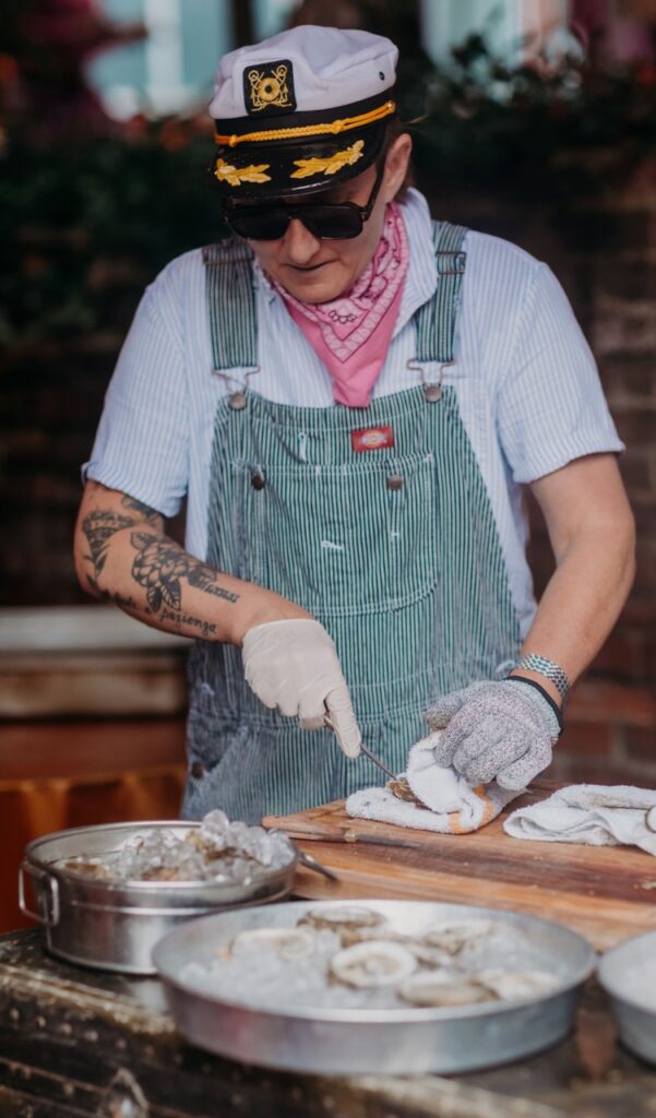 A person in a captain's hat shucks oysters.