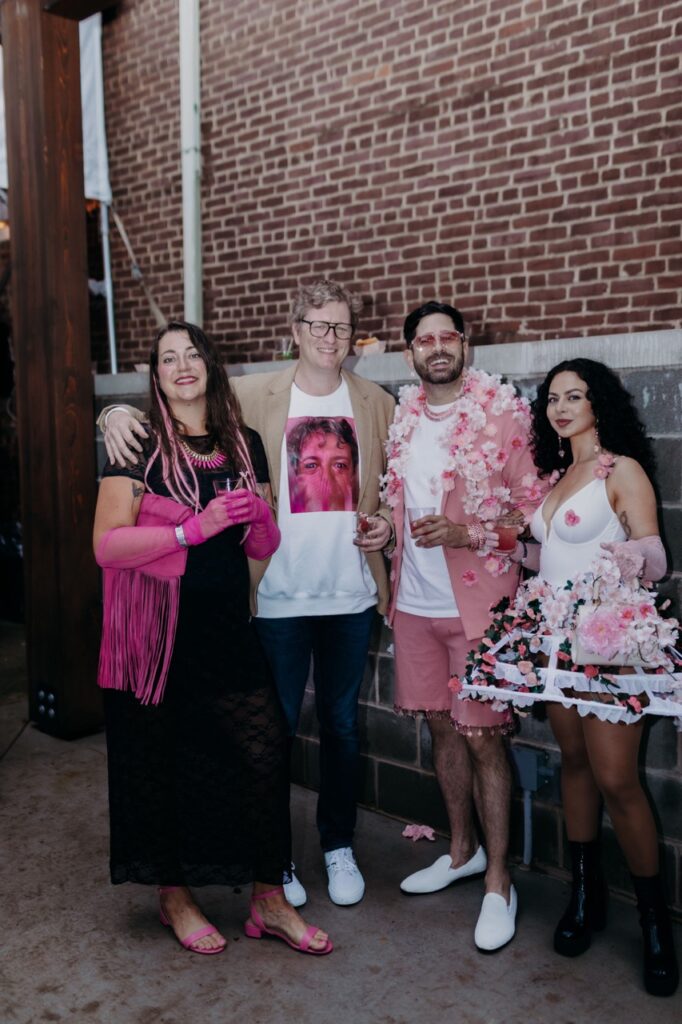 A group of two men and two women in pink clothes stand against a brick wall together.