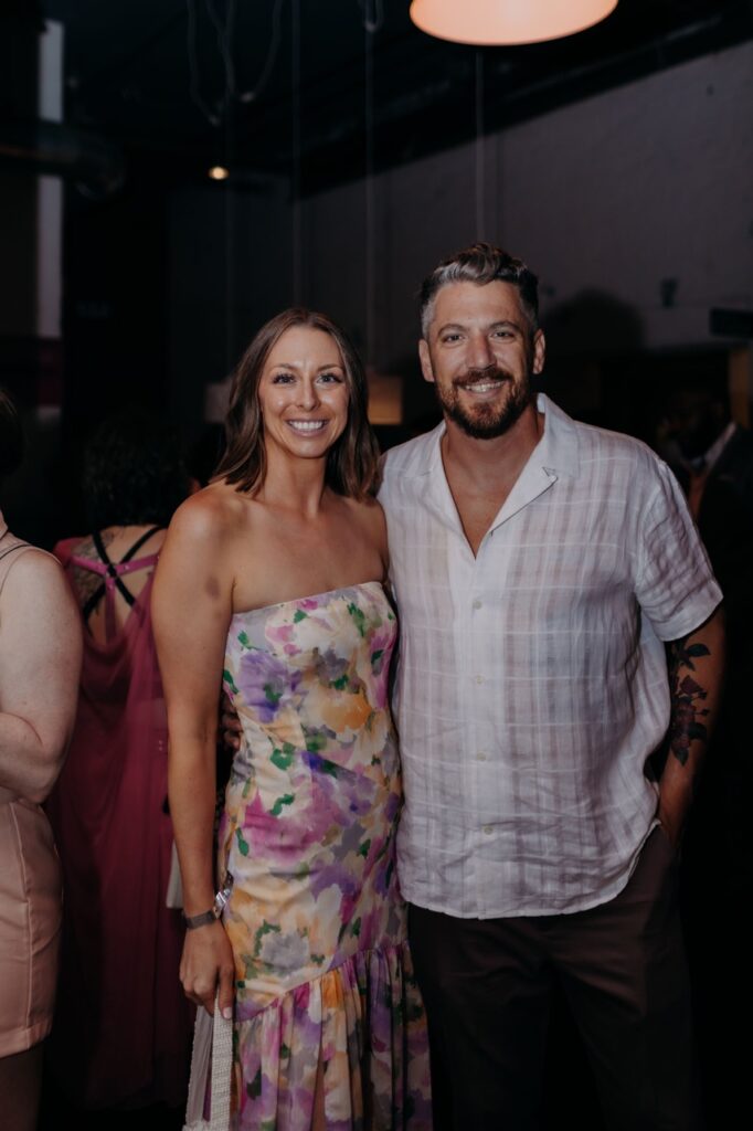 A woman in a floral dress and a man in a white button up shirt smile together.