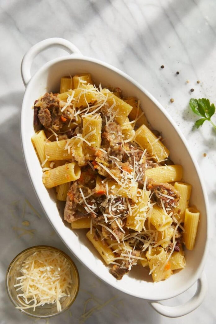 A white serving dish filled with rigatoni pasta and a rich Genovese sauce, topped with grated cheese.