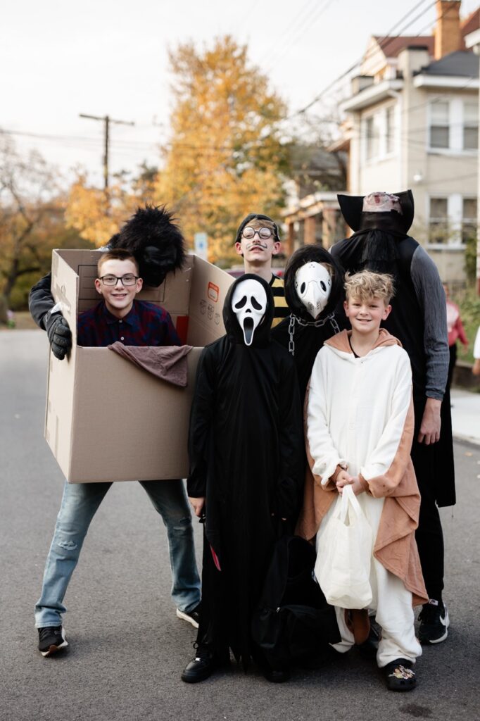 A group of kids in Halloween costumes stand in the street.