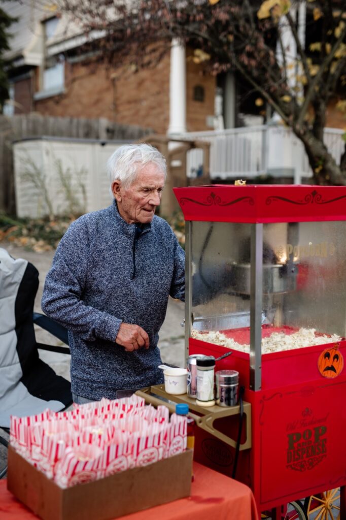 An older man makes popcorn in a machine outside.