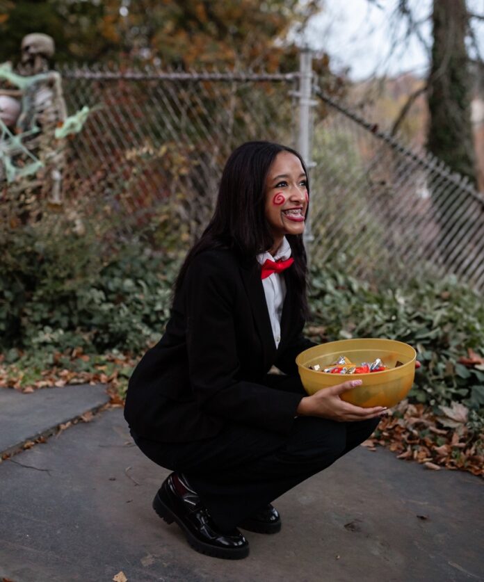 A woman crouches with a bowl of candy outside.