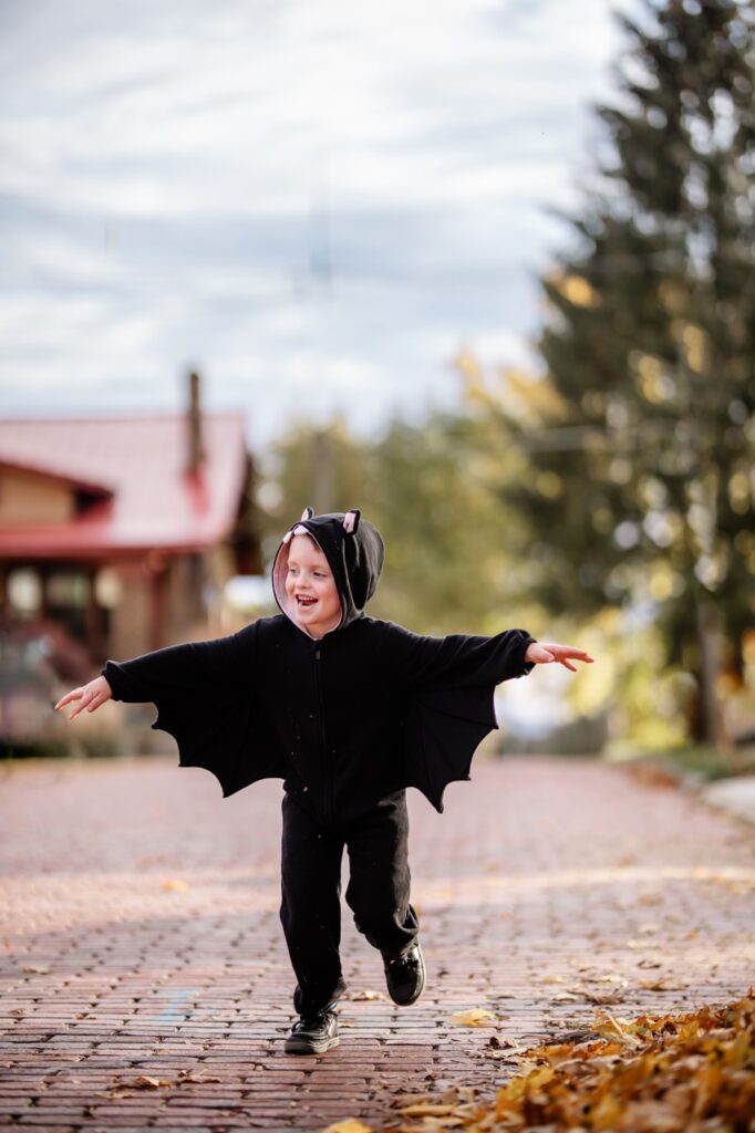 A little kid in a bat costume runs down a brick road.