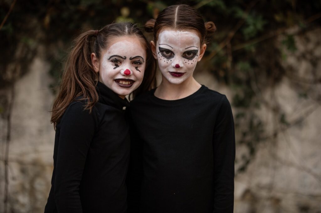 Two little girls dressed in black as clowns stand together.