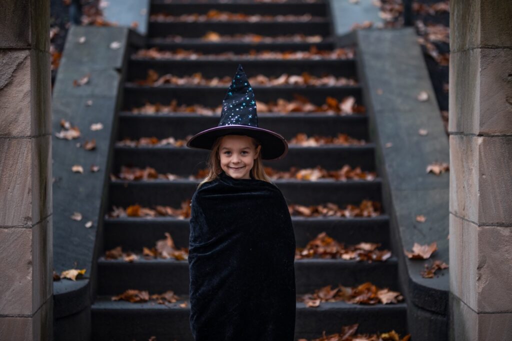A little girl dressed as a witch in front of stairs.