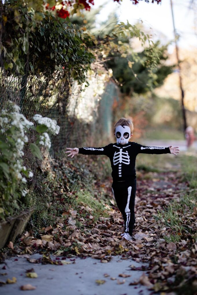 A little boy walks with his arms outstretched dressed as a skeleton.