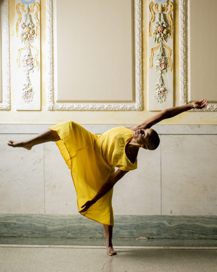 A woman dances in a yellow dress with her arms and legs outstretched.