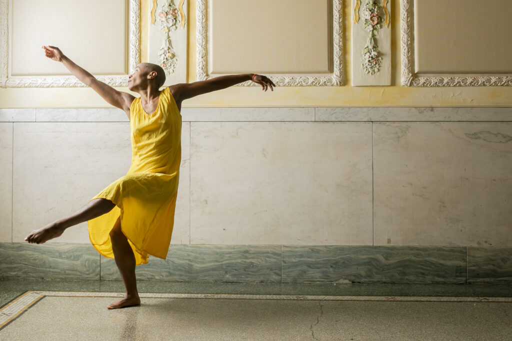 A woman kicks her foot up while dancing and stretches her arms out.