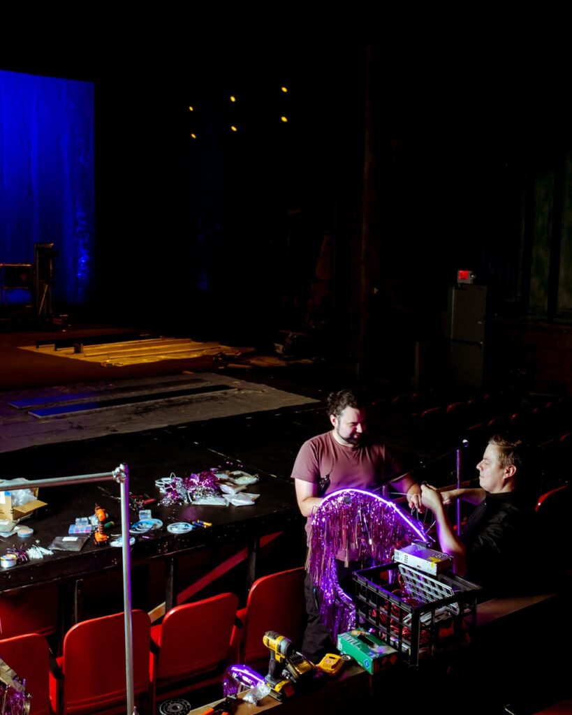 Two men work together in red theater seats to build production.