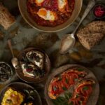 A collection of tartines and a bowl of kimshuka, featuring different toppings like poached pears, tomatoes, and a savory greens mixture.