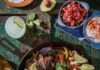 8 Chicken Recipes to Help Keep Dinner Affordable in 2026 A chicken fajita skillet with slices chicken, limes, and peppers. Then there are small bowls of pico, sour cream, and onions.