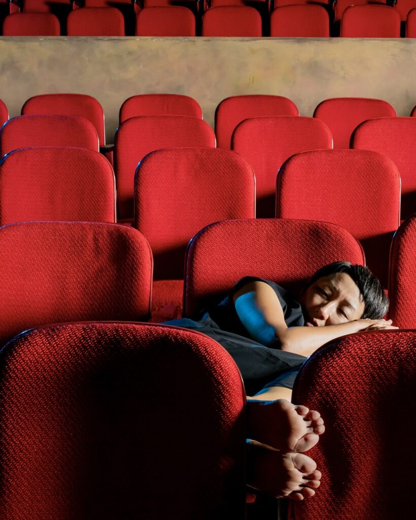 Dancer Maree ReMalia curls up in a red theater chair.