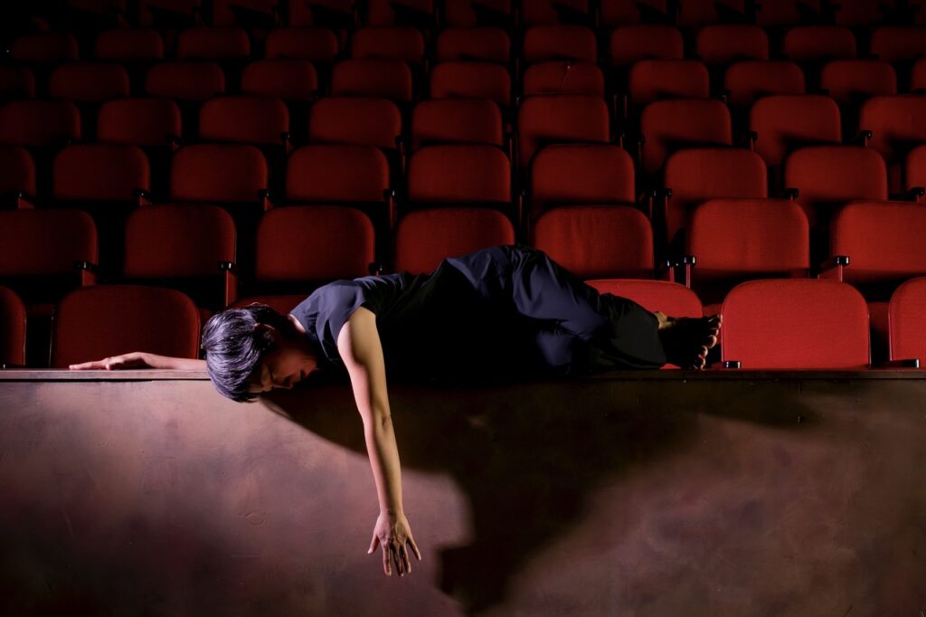 A woman lays in front of rows of red theater seats.