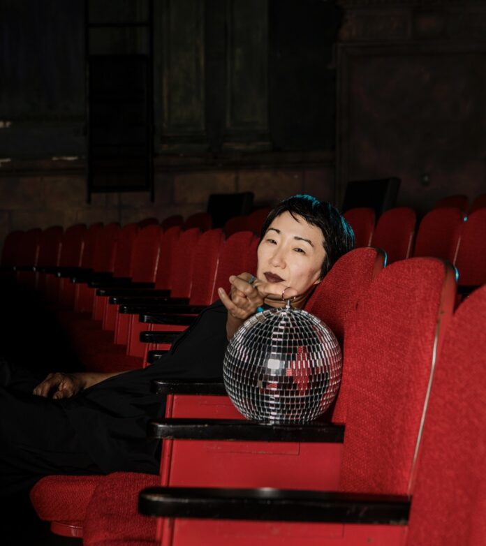 Maree ReMalia sits in a red velvet seat with a disco ball in front of her.