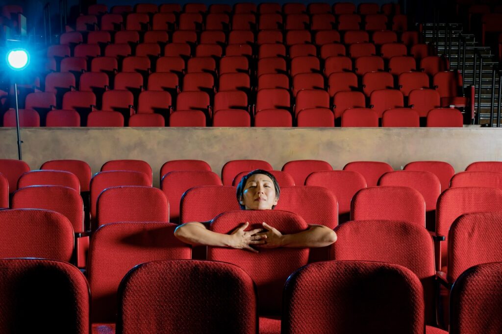 A woman sitting in a theater seat wraps her arms around it.