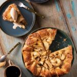 On a dark plate sits an Apple Crostada inspired by Martha Stewart which is made with a cheddar cheese crust. One slice has been cut out and sits on another plate with a scoop of ice cream on top.