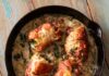 Martha Stewart-Inspired Keto Chicken Roll Ups A cast iron pan on a picnic table with chicken roll ups sitting in a creamy sauce with two small containers of salt and pepper below.