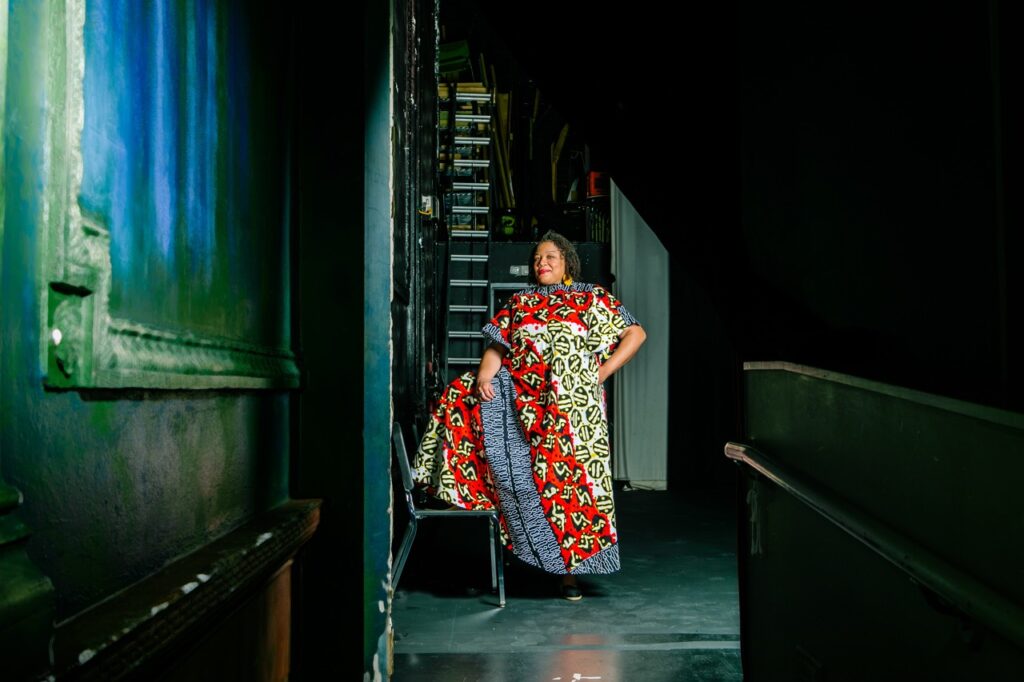A woman stands back stage with her foot on a chair.