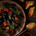A delectable seafood dish featuring mussels, sausage, and broccolini, crafted by Chef Don Winkie of 80 Acres restaurant.